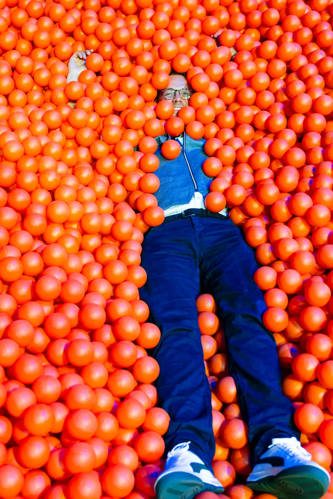 Jens Issel liegt lachend und rücklings in einem Bällebad voller orangefarbener Bälle