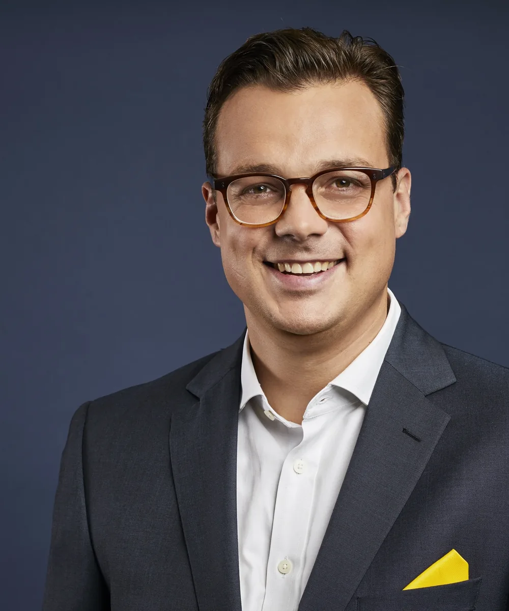 Jens Issel im dunklen Anzug mit gelbem Einstecktuch, lächelnd